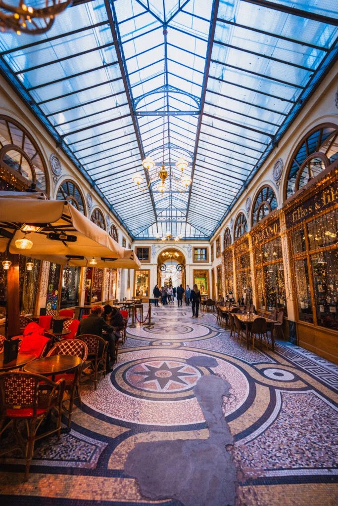 Galerie Vivienne, via 6 rue Vivienne, 75002 Paris. Stop beside the mosaic floor in the open passage, leaving space for people to pass.