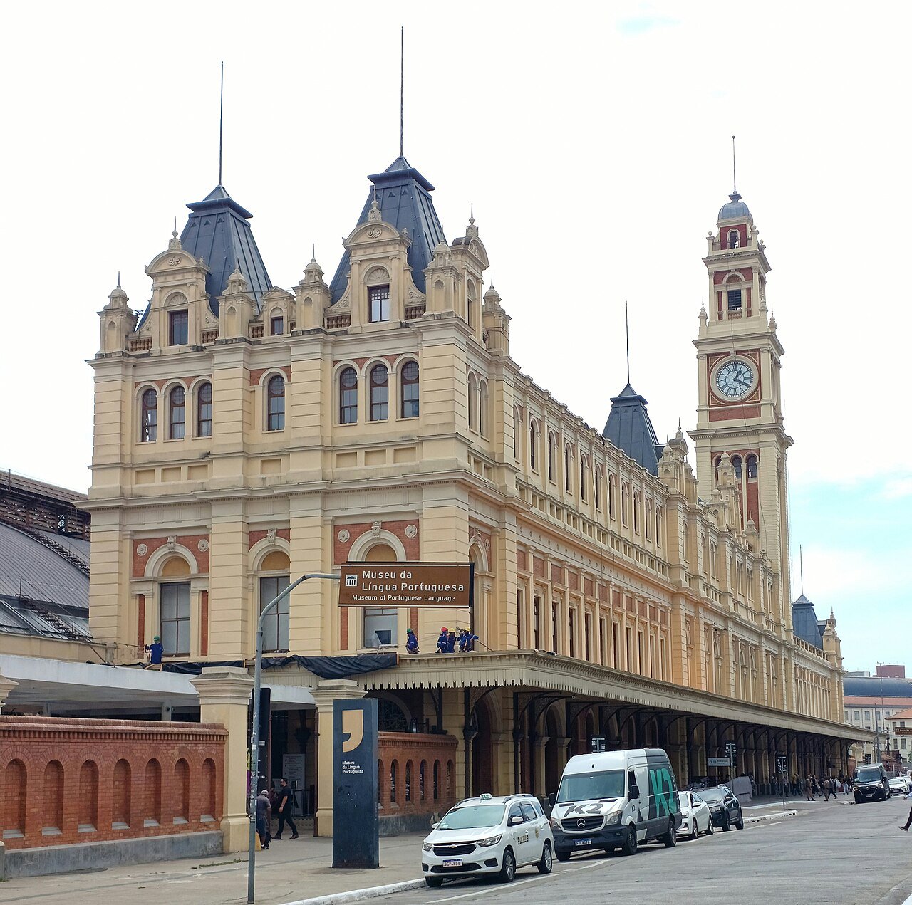 Public pavement on Praça da Luz facing the historic Luz Station clock tower, outside the station doors and passenger flow.