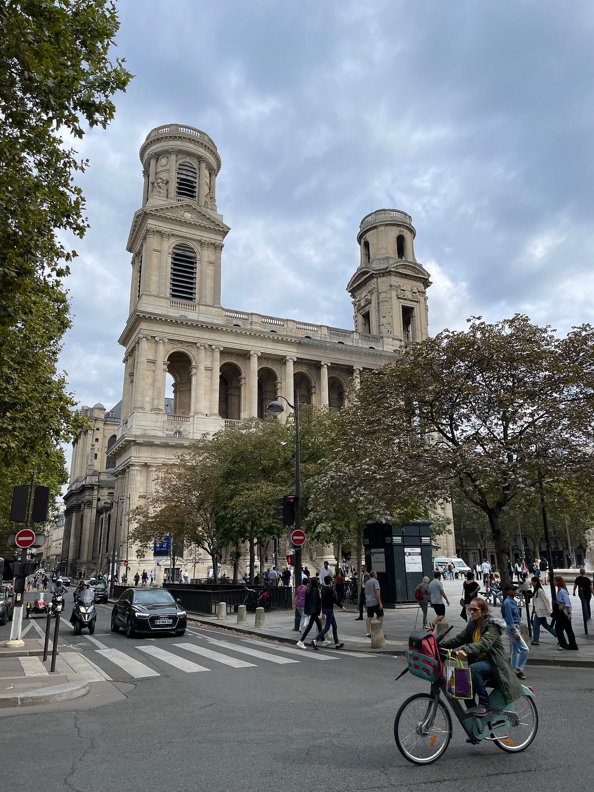Public space on place Saint-Sulpice with both church towers in view, 75006 Paris. Keep pedestrian routes and the fountain edge clear.