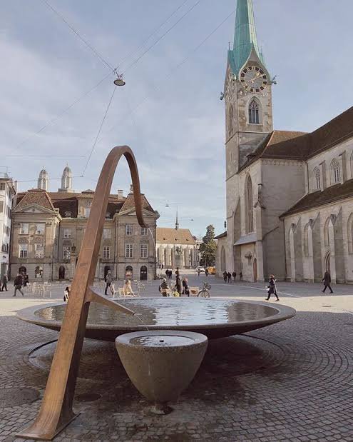 Public square beside the Münsterhof fountain, clear of its basin and passing pedestrians.