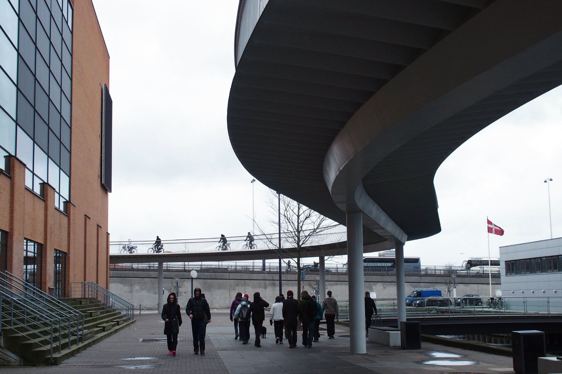 Ground-level public pedestrian quay beside Cykelslangen at Havneholmen, below the elevated route and set back from the water.