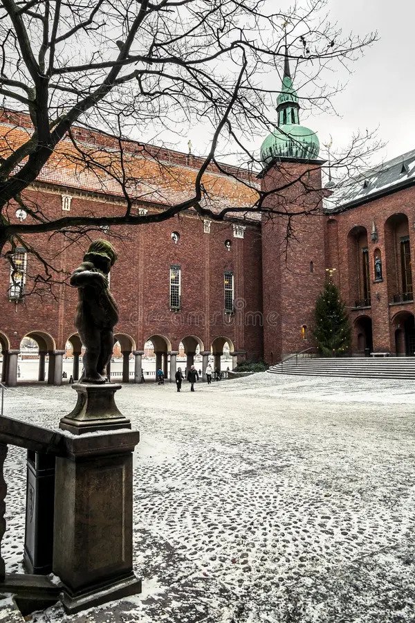 Public paving in Borgargården, the City Hall courtyard. Face the crowned figure above the archway from the open courtyard, leaving doors and tour groups room to pass.